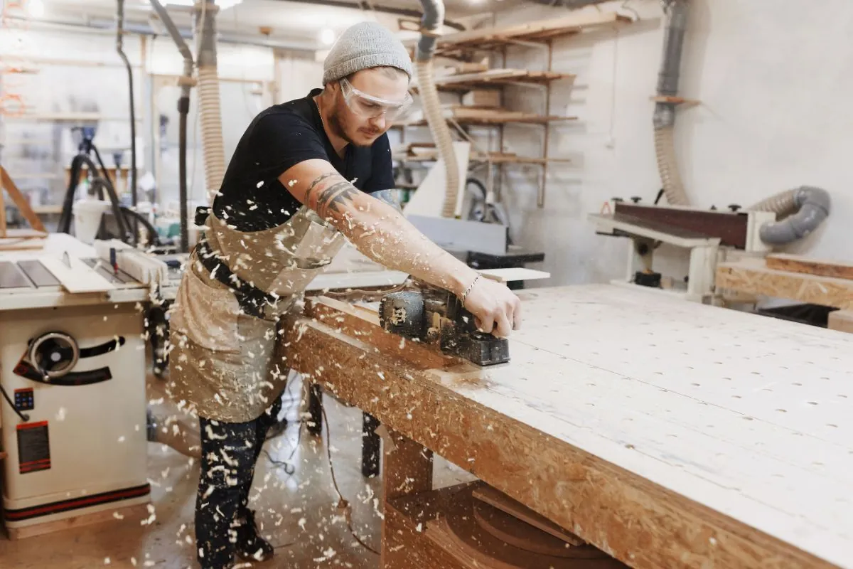 carpenter working with electric planer on wooden plank in workshop